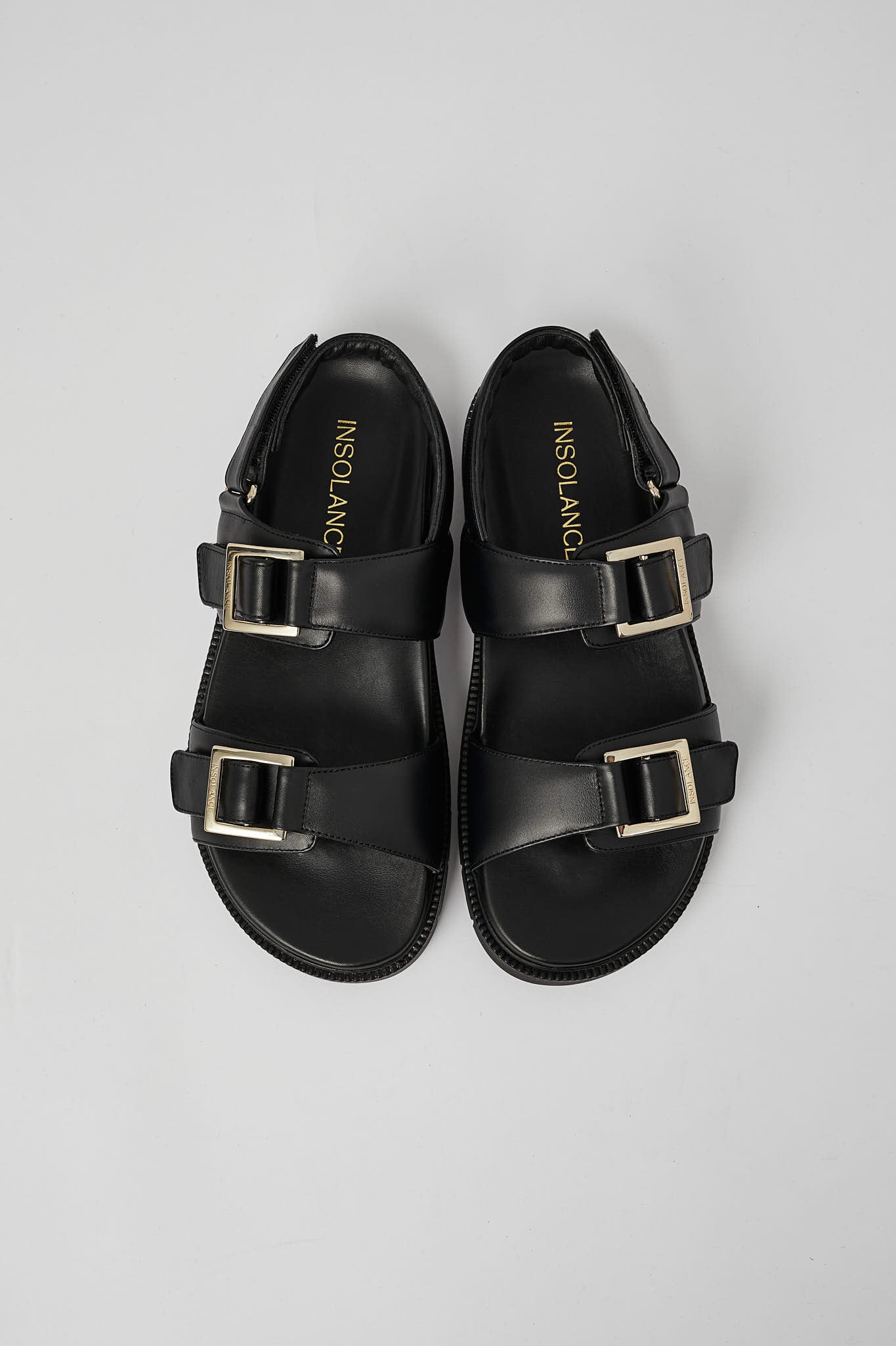 Sandalias Barna negras de cuero con hebillas doradas sobre fondo gris claro