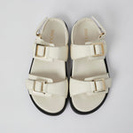 Pair of white sandals with gold buckles on a light gray background