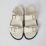 Pair of white sandals with gold buckles on a light gray background