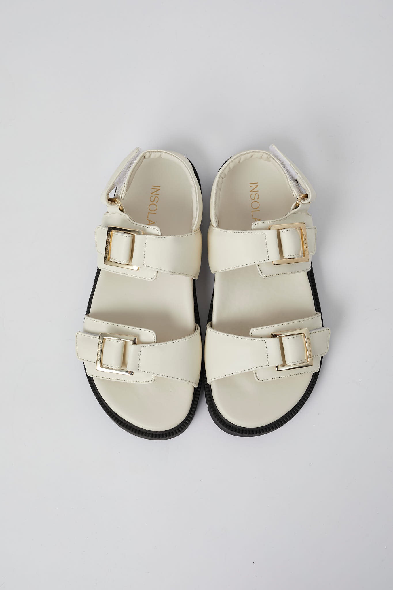 Pair of white sandals with gold buckles on a light gray background